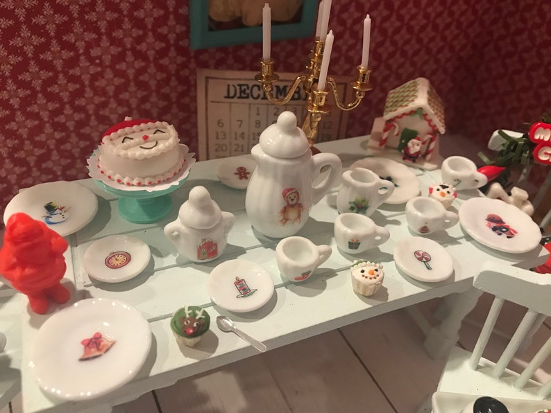 May include: A miniature Christmas-themed table setting with a Santa cake, teapot, cups, and plates. The plates feature festive designs like snowmen and candles. A gingerbread house and a December calendar are also present.