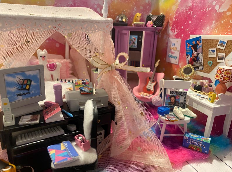 K&ouml;nnte beinhalten: Ein Miniatur-Puppenhaus-Schlafzimmer mit einem rosa Himmelbett, einem Computertisch mit Monitor, Tastatur und Drucker, einem Schminktisch mit Spiegel und Make-up sowie einem rosa-wei&szlig;en Teppich. Das Zimmer ist mit Sternen und anderen m&auml;dchenhaften Details dekoriert.