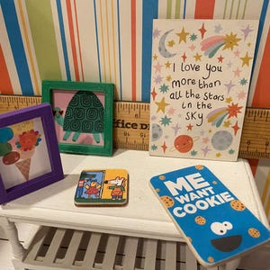 May include: A collection of miniature art pieces and decorative items. Includes a framed ice cream cone, a framed turtle, a coaster with a cartoon scene, a card with the text "I love you more than all the stars in the sky", and a "Me Want Cookie" sign.