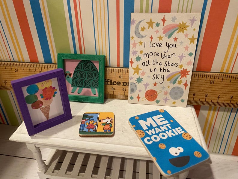May include: A collection of miniature art pieces and decorative items. Includes a framed ice cream cone, a framed turtle, a coaster with a cartoon scene, a card with the text "I love you more than all the stars in the sky", and a "Me Want Cookie" sign.