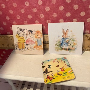 Puede incluir: Tres impresiones art&iacute;sticas cuadradas de estilo vintage. Una muestra gatitos vestidos, otra un conejito con una chaqueta azul y la tercera un dise&ntilde;o de mariposas. La impresi&oacute;n de los gatitos muestra tres gatitos. La impresi&oacute;n del conejito representa un conejito.