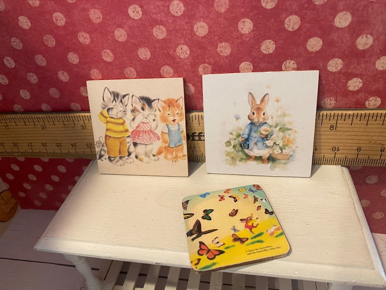 Puede incluir: Tres impresiones art&iacute;sticas cuadradas de estilo vintage. Una muestra gatitos vestidos, otra un conejito con una chaqueta azul y la tercera un dise&ntilde;o de mariposas. La impresi&oacute;n de los gatitos muestra tres gatitos. La impresi&oacute;n del conejito representa un conejito.