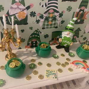 Puede incluir: Una mesa blanca con un candelabro dorado, cuatro ollas verdes llenas de monedas de oro, un arcoíris y un libro titulado "Cómo atrapar un duende". La mesa está decorada con monedas de oro y tréboles verdes. El fondo es un patrón verde y blanco con gnomos.