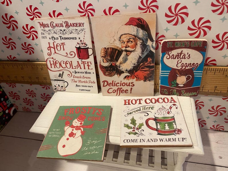 Pode incluir: Cinco placas de madeira de estilo vintage com designs natalinos. As placas apresentam ilustra&ccedil;&otilde;es do Papai Noel, chocolate quente, ponche de ovos e um boneco de neve. As placas s&atilde;o nas cores vermelho, branco e verde e incluem texto como "Chocolate quente", "Ponche de ovos do Papai Noel" e "Chocolate quente".