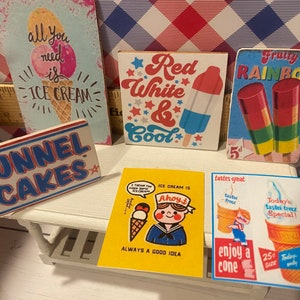 May include: A collection of vintage-style ice cream and dessert-themed signs. The signs feature phrases like "Funnel Cakes," "Red White & Cool," and "All you need is Ice Cream." The color palette includes red, white, blue, yellow, and pastel tones.
