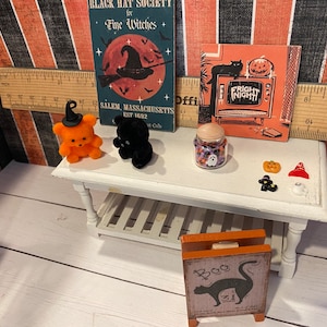 May include: A miniature Halloween scene with an orange teddy bear wearing a witch's hat, a black teddy bear, a glass jar filled with candy, and a sign that says "Boo".