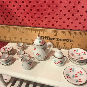 Puede incluir: Un juego de t&eacute; en miniatura con estampado de cerezas que incluye una tetera, una jarra de crema, un azucarero, tazas y platillos. El juego es blanco con cerezas rojas y hojas verdes.