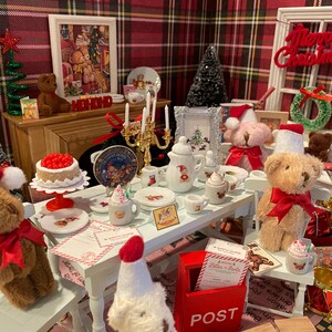 Puede incluir: Una escena navide&ntilde;a en miniatura con osos de peluche, un pastel y una mesa. Los osos llevan gorros de Pap&aacute; Noel y lazos rojos. La mesa est&aacute; puesta con platos, tazas y una tetera. Una imagen enmarcada y un &aacute;rbol de Navidad est&aacute;n en el fondo.