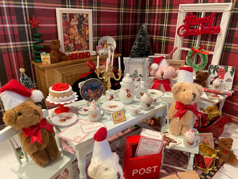 Puede incluir: Una escena navide&ntilde;a en miniatura con osos de peluche, un pastel y una mesa. Los osos llevan gorros de Pap&aacute; Noel y lazos rojos. La mesa est&aacute; puesta con platos, tazas y una tetera. Una imagen enmarcada y un &aacute;rbol de Navidad est&aacute;n en el fondo.