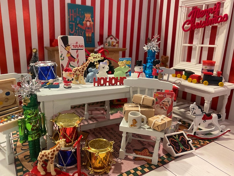 May include: A miniature Christmas scene with various toys and decorations. Includes a toy soldier, drums, a giraffe, and a rocking horse. The scene is set against a red and white striped background, with a "Merry Christmas" sign.