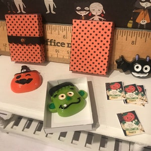 Puede incluir: Una escena de Halloween en miniatura con una mesa blanca, dos cajas de lunares naranja y negro, una calabaza con un sombrero de bruja, una cara verde de Frankenstein, un murci&eacute;lago negro y cuatro invitaciones que dicen "Est&aacute;s invitado a una fiesta de Halloween".