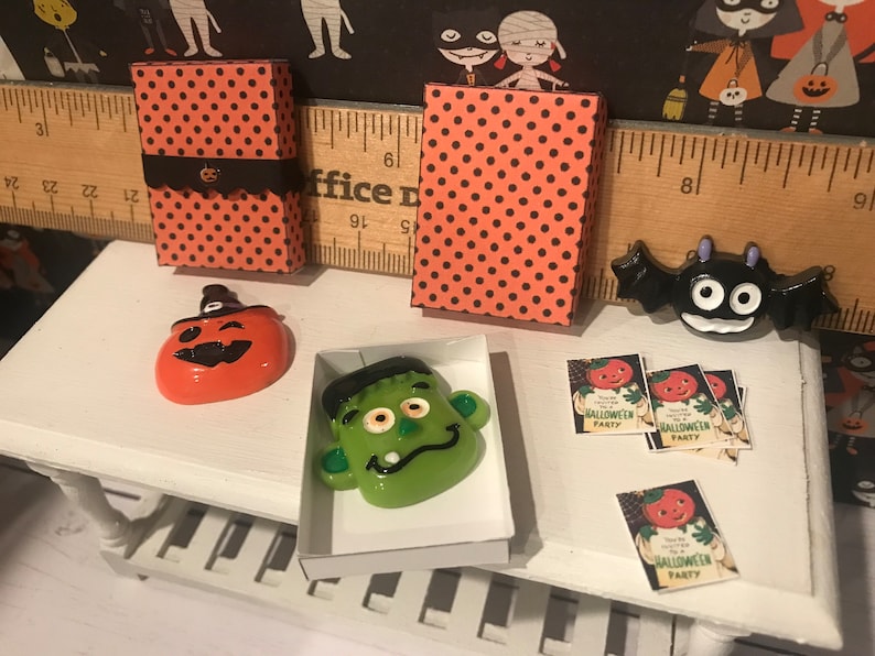 Puede incluir: Una escena de Halloween en miniatura con una mesa blanca, dos cajas de lunares naranja y negro, una calabaza con un sombrero de bruja, una cara verde de Frankenstein, un murci&eacute;lago negro y cuatro invitaciones que dicen "Est&aacute;s invitado a una fiesta de Halloween".