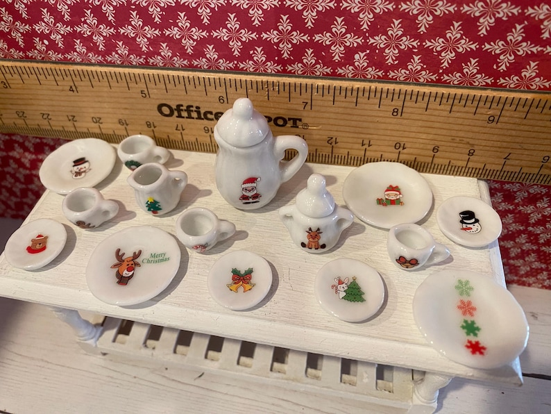 May include: A miniature Christmas-themed tea set. The white porcelain set includes a teapot, creamer, sugar bowl, cups, and saucers. Each piece is decorated with festive images of Santa, snowmen, reindeer, and Christmas trees.