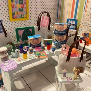 May include: Miniature scene featuring baby care products, including Pampers boxes, baby food jars, and a bib. Several tote bags with brown handles are present, along with small toys and decorative items. The scene is set on a white table and a small stool.