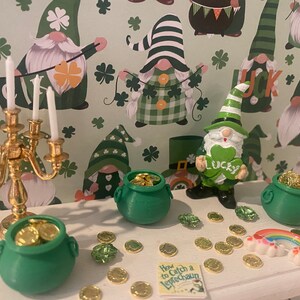 Puede incluir: Una mesa blanca con un candelero dorado, tres ollas de oro verdes, un arco&iacute;ris y un libro titulado "C&oacute;mo atrapar un duende". La mesa est&aacute; decorada con monedas de oro y tr&eacute;boles verdes. El fondo es un patr&oacute;n verde y blanco con gnomos que llevan sombreros verdes.