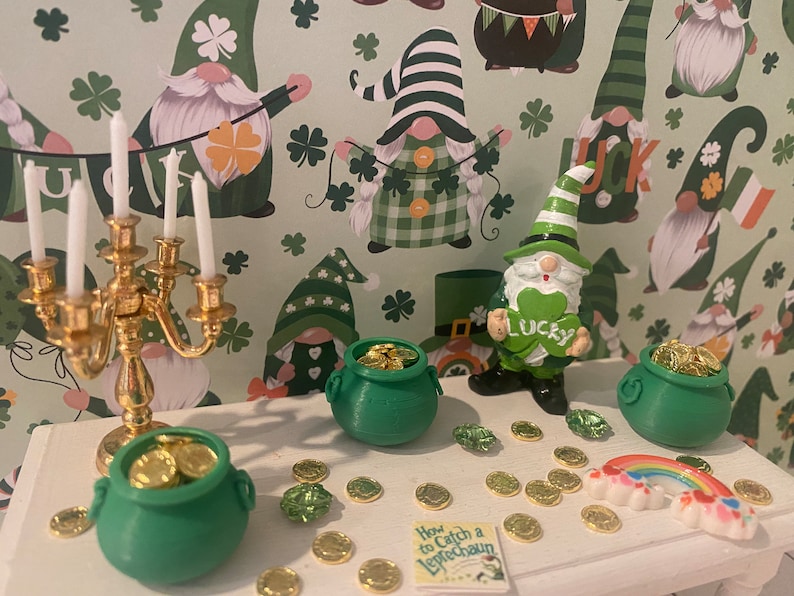 Puede incluir: Una mesa blanca con un candelero dorado, tres ollas de oro verdes, un arco&iacute;ris y un libro titulado "C&oacute;mo atrapar un duende". La mesa est&aacute; decorada con monedas de oro y tr&eacute;boles verdes. El fondo es un patr&oacute;n verde y blanco con gnomos que llevan sombreros verdes.
