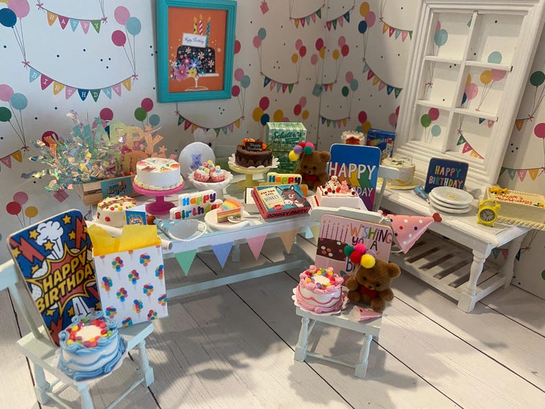 May include: A miniature birthday party scene with several cakes, teddy bears, and decorations. The scene includes a framed picture of a cake, a table with various treats, and a small chair with a cake on it. The background features a wallpaper with balloons and banners.