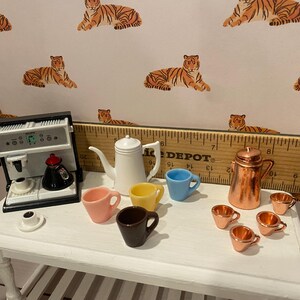 Pode incluir: Conjunto de caf&eacute; em miniatura com uma m&aacute;quina de espresso branca, uma chaleira branca e v&aacute;rias x&iacute;caras coloridas. Uma cafeteira de cobre e x&iacute;caras combinando tamb&eacute;m est&atilde;o presentes. O fundo apresenta um papel de parede com estampa de tigre.