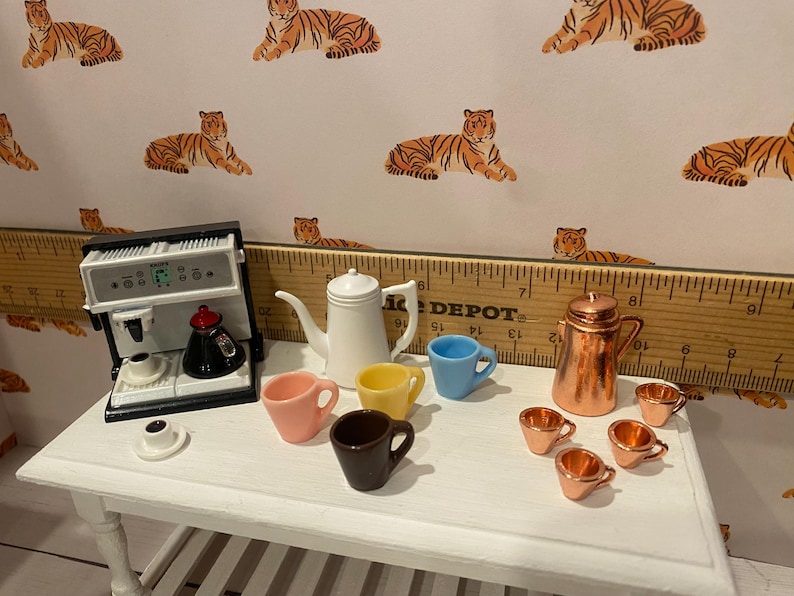 Pode incluir: Conjunto de caf&eacute; em miniatura com uma m&aacute;quina de espresso branca, uma chaleira branca e v&aacute;rias x&iacute;caras coloridas. Uma cafeteira de cobre e x&iacute;caras combinando tamb&eacute;m est&atilde;o presentes. O fundo apresenta um papel de parede com estampa de tigre.