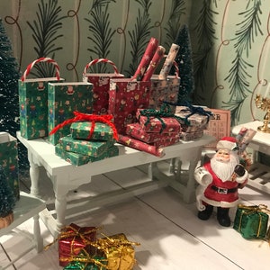 Puede incluir: Una escena navide&ntilde;a en miniatura con una figura de Pap&aacute; Noel, un peque&ntilde;o &aacute;rbol de Navidad y una mesa llena de regalos envueltos y bolsas de regalo. Los regalos est&aacute;n envueltos en papel de regalo navide&ntilde;o festivo con dise&ntilde;os de Pap&aacute; Noel, renos y otros motivos navide&ntilde;os.