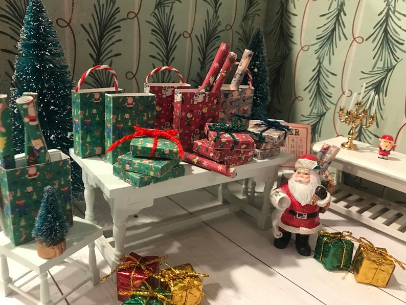 Puede incluir: Una escena navide&ntilde;a en miniatura con una figura de Pap&aacute; Noel, un peque&ntilde;o &aacute;rbol de Navidad y una mesa llena de regalos envueltos y bolsas de regalo. Los regalos est&aacute;n envueltos en papel de regalo navide&ntilde;o festivo con dise&ntilde;os de Pap&aacute; Noel, renos y otros motivos navide&ntilde;os.