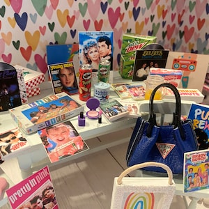 Puede incluir: Una colección de artículos en miniatura con temática de los años 80 y 90, que incluye un disco de Prince morado, un juego de mesa Life, una lata de Pringles, una loción de Bath & Body Works, un bolso Guess, una revista de Punky Brewster, una revista de Brady Bunch y un póster de la película Pretty in Pink.