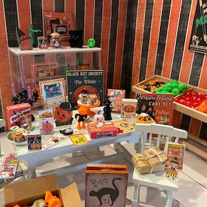 May include: A miniature Halloween shop with a white table and chairs, a display case with candles and a black cat, a wooden stand with orange and red candy, and various Halloween-themed decorations, including a sign that reads "Black Hat Society Fine Witches" and a sign that reads "Fortune Telling Cake Set".
