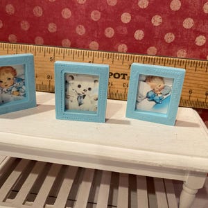Puede incluir: Tres peque&ntilde;os marcos de fotos azul claro con im&aacute;genes de estilo vintage. Un marco presenta un beb&eacute; con un osito de peluche, otro un osito de peluche y el tercero un beb&eacute; con un osito de peluche. Los marcos se exhiben sobre una mesa blanca.