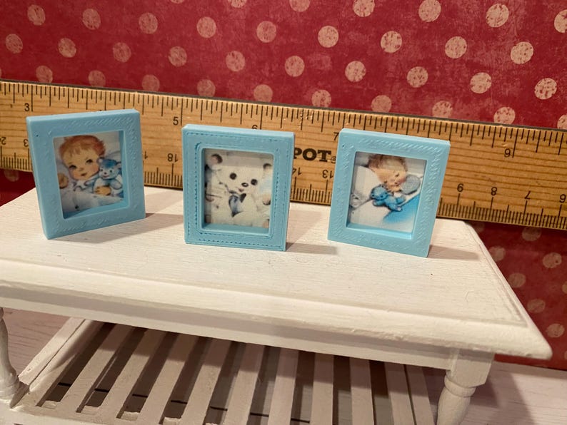 Puede incluir: Tres peque&ntilde;os marcos de fotos azul claro con im&aacute;genes de estilo vintage. Un marco presenta un beb&eacute; con un osito de peluche, otro un osito de peluche y el tercero un beb&eacute; con un osito de peluche. Los marcos se exhiben sobre una mesa blanca.