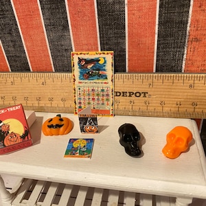 May include: A miniature Halloween scene with a trick-or-treat box, a pumpkin, a Halloween card, a black skull, an orange skull, and a vintage Halloween calendar with the text "1954 OCTOBER 1954".
