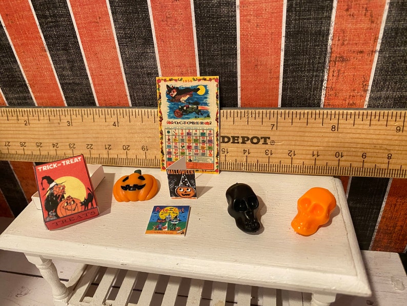 May include: A miniature Halloween scene with a trick-or-treat box, a pumpkin, a Halloween card, a black skull, an orange skull, and a vintage Halloween calendar with the text "1954 OCTOBER 1954".