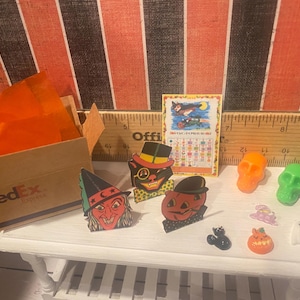 May include: A collection of vintage Halloween decorations, including a witch, a black cat, a pumpkin, and a ghost. There are also a few small plastic skulls and a ruler in the background.