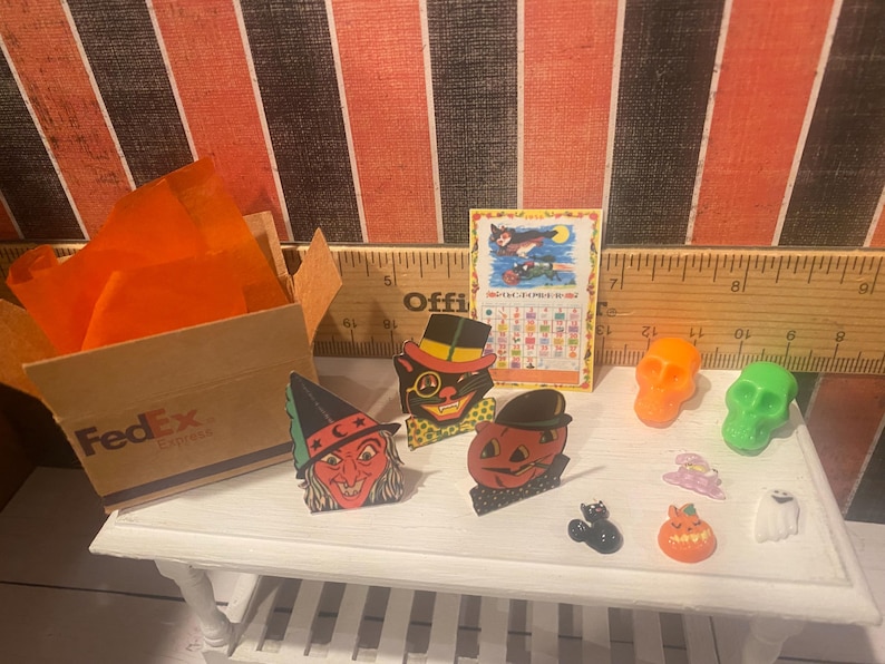 May include: A collection of vintage Halloween decorations, including a witch, a black cat, a pumpkin, and a ghost. There are also a few small plastic skulls and a ruler in the background.