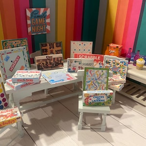 May include: A collection of miniature board games, such as Monopoly, Cluedo, Scrabble, and Sorry!, are arranged on a white table. Other games include Chutes and Ladders, Candy Land, and Twister. The background features a colourful striped wall and a sign that reads "Family Game Night."