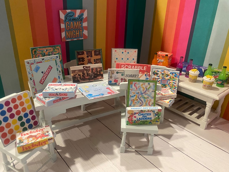 May include: A collection of miniature board games, such as Monopoly, Cluedo, Scrabble, and Sorry!, are arranged on a white table. Other games include Chutes and Ladders, Candy Land, and Twister. The background features a colourful striped wall and a sign that reads "Family Game Night."