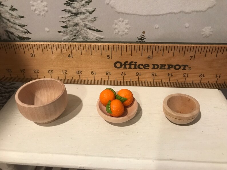 May include: Three miniature wooden bowls, one filled with three orange-colored miniature oranges, and two empty bowls. The bowls are on a white surface with a wooden ruler behind them. The ruler is labeled "Office Depot".