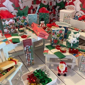 Puede incluir: Una colección de suministros de envoltura de regalos navideños en miniatura que incluye bolsas de regalo estampadas, rollos de papel de regalo, cintas rojas y verdes, lazos metálicos, una pequeña figura de Santa Claus y un calendario en miniatura de diciembre de 1947.