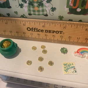 Puede incluir: Una olla verde llena de monedas de oro, un arco&iacute;ris, un tr&eacute;bol de cuatro hojas y un libro titulado "How to Catch a Leprechaun" sobre una superficie blanca. Tambi&eacute;n hay varias monedas de oro esparcidas alrededor de la olla.