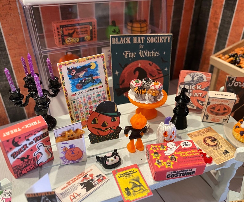 May include: A miniature Halloween scene with a black candlestick, a calendar, a sign that reads "Black Hat Society for Fine Witches", a box of "Trick or Treat" candy, and a variety of Halloween-themed decorations.