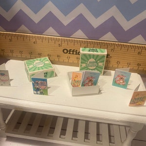 May include: A set of miniature Easter cards and a box with the text "Happy Easter" on it. The cards feature various Easter themes, including bunnies, chicks, and eggs. The box is green and white with a green and white checkered pattern.