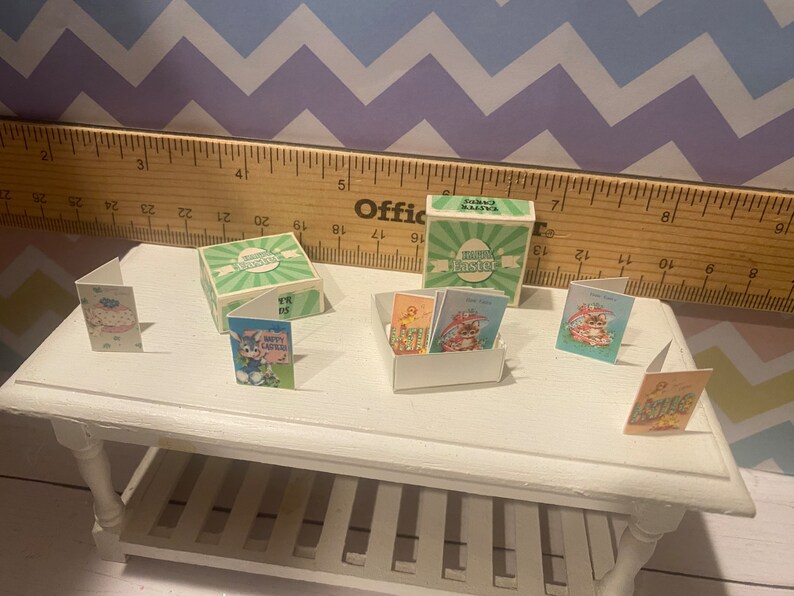 May include: A set of miniature Easter cards and a box with the text "Happy Easter" on it. The cards feature various Easter themes, including bunnies, chicks, and eggs. The box is green and white with a green and white checkered pattern.