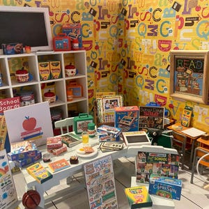 Peut inclure: Une diorama miniature sur le thème de l'école avec un tableau noir, des étagères remplies de nourriture et des fournitures scolaires. La scène comprend une pancarte indiquant « Back to School Bulletin Boards » et une pancarte indiquant « Eat the Rainbow Every Day ! » Un ballon de basket est au sol.