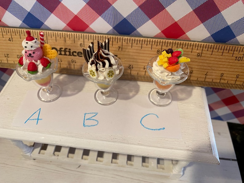 May include: Miniature dessert sundaes in clear glass dishes. One sundae has a pink bear, strawberries, and a red and white striped candy cane. Another has chocolate sauce and chocolate sticks. The third has fruit.