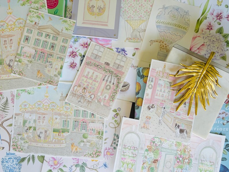 May include: A collection of illustrated art prints featuring whimsical scenes with dogs, including buildings, a carousel, and a hot air balloon. The prints have a pastel color palette with floral and architectural elements, and a gold leaf decoration.