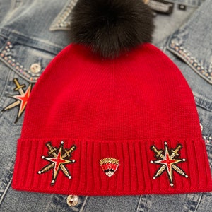 May include: Red knit beanie with a black pom pom and gold and red embroidered star and sword designs.