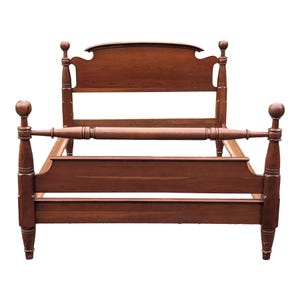May include: A wooden bed frame with a rich brown finish, featuring a tall headboard with a curved top rail, a lower footboard, and four vertical posts topped with spherical finials. The frame includes side rails and a horizontal support bar.