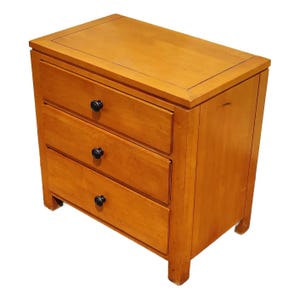 May include: A three-drawer wooden nightstand with a light wood finish and black drawer pulls.
