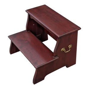 May include: A two-step wooden step stool with a rich, dark cherry finish. The stool features a rectangular top step and a lower step, connected by a sturdy frame. A brass-colored handle is attached to the side.