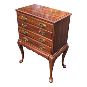 May include: A wooden chest of drawers featuring a rich brown finish, four horizontal drawers, and brass-toned metal pulls. The piece is supported by four curved cabriole legs that terminate in pad feet, showcasing a rectangular top surface.