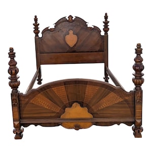 May include: A dark brown antique bed frame with ornate detailing. The headboard features a decorative shield-shaped inlay and a curved top. The footboard has a sunburst design. The bed has four tall, carved posts.